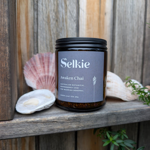 Selkie tea labeled 'Awaken Chai' on a wooden surface with seashells and plants.
